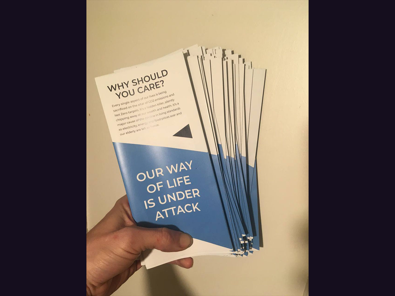 A hand holding a stack of The Climate Con A4 trifold leaflets