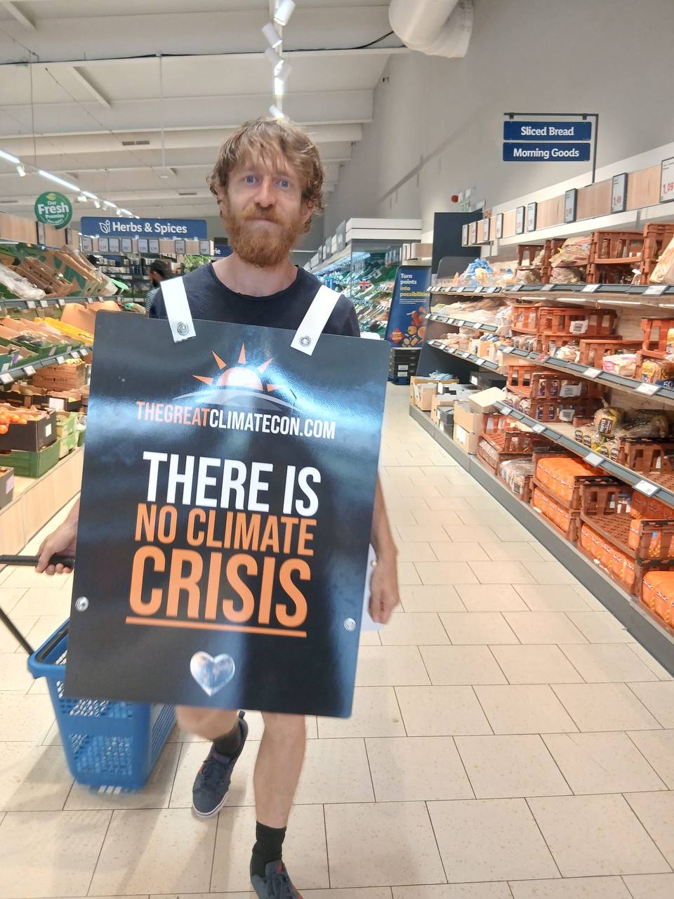 Travis Cook wearing the THEGREATCLIMATECON.COM "There is no climate crisis" sandwich board in a supermarket